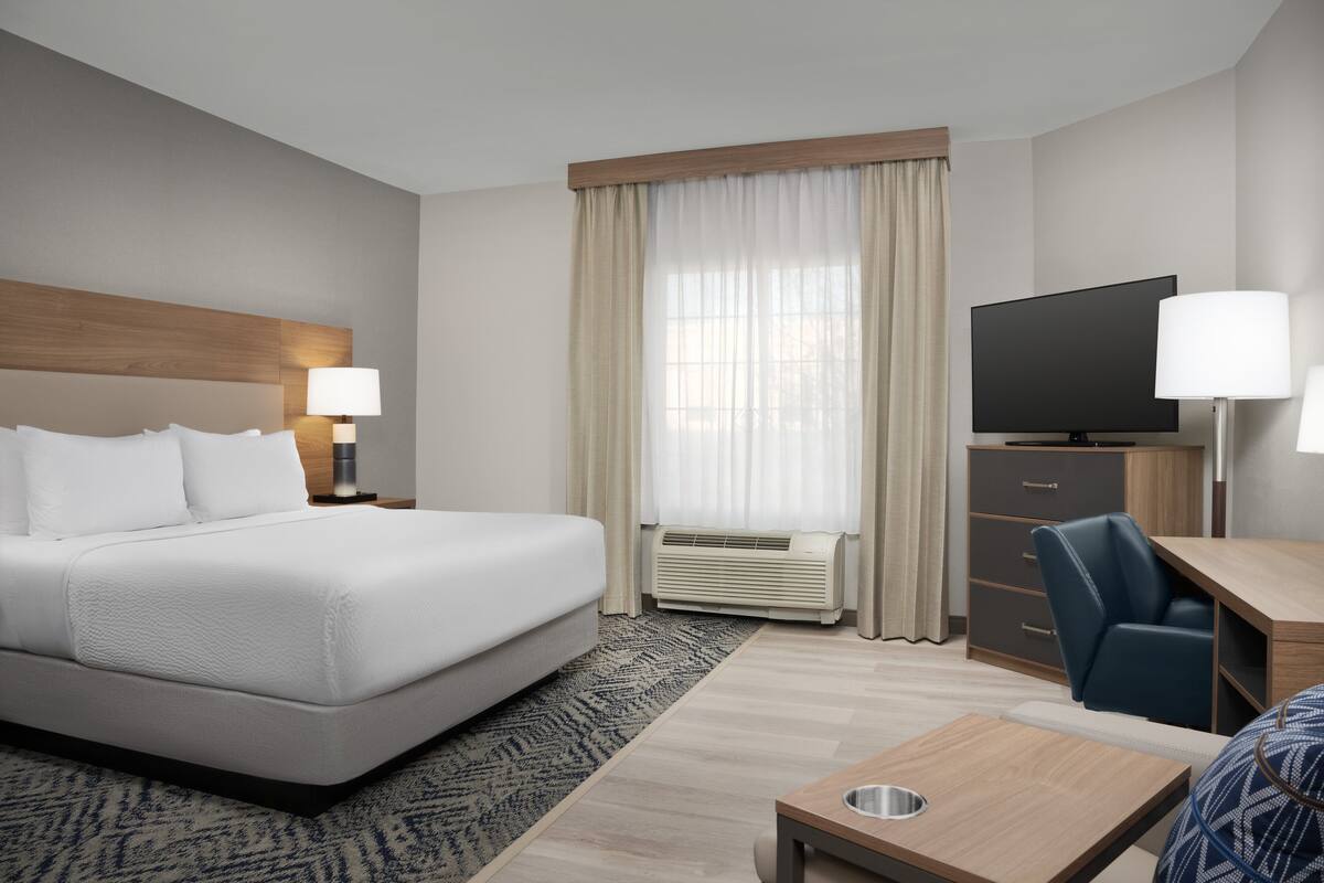 A hotel room with a large bed, a desk with a chair, a television, and a window with curtains.