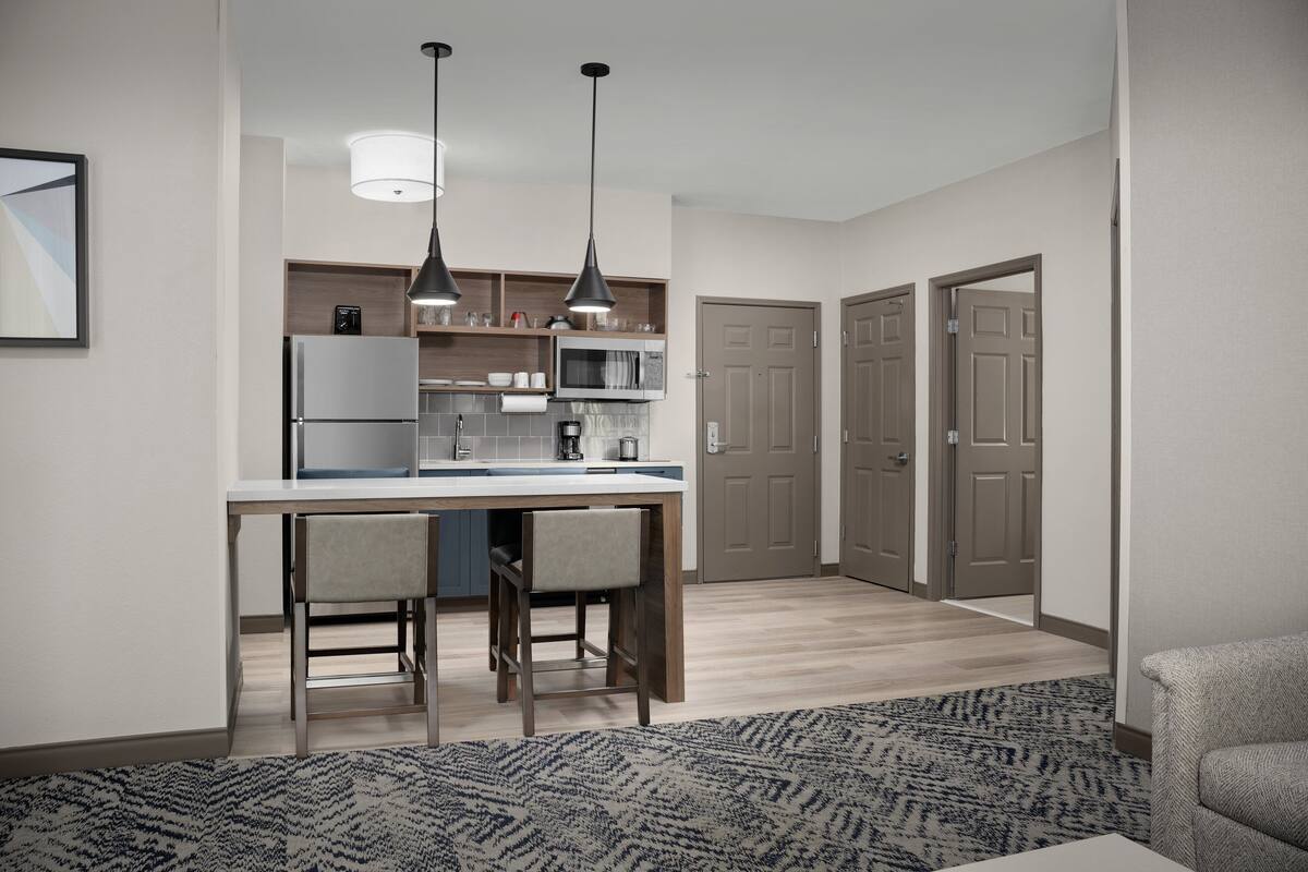 A modern kitchen with a refrigerator, microwave, and dining area with two chairs. There are two pendant lights above the counter.