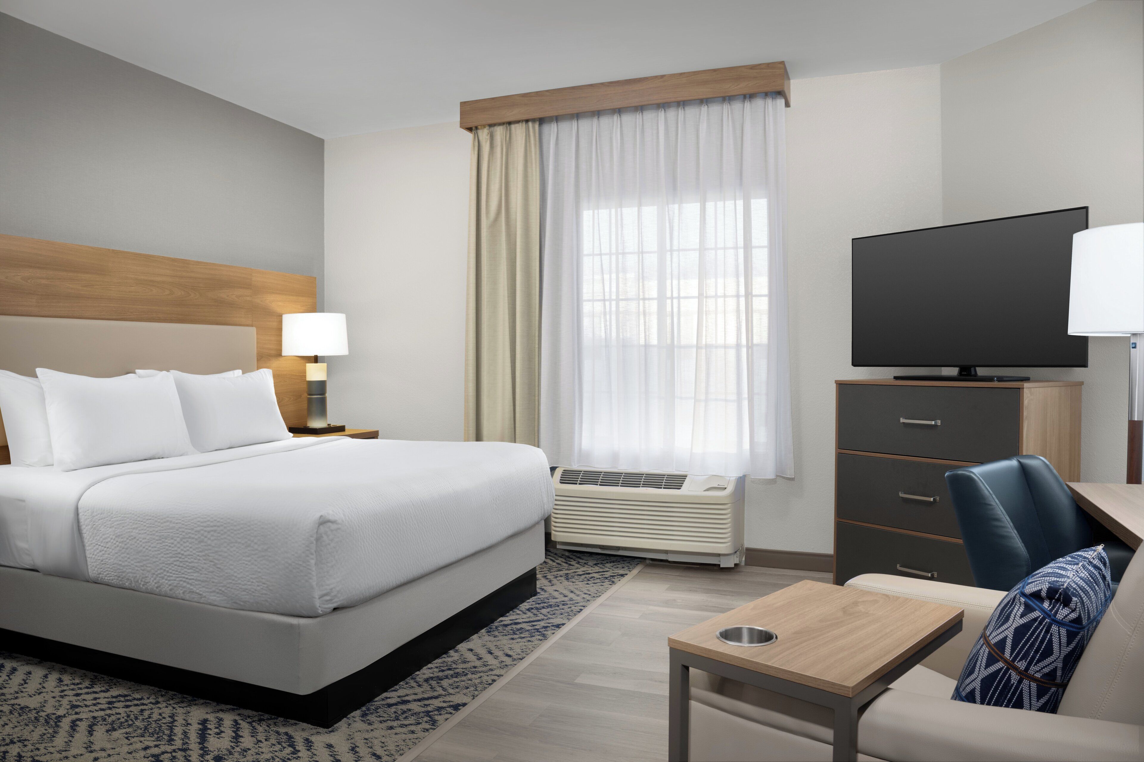 Une chambre d’hôtel avec un lit, un bureau, une chaise, une télévision et une fenêtre avec des rideaux.
