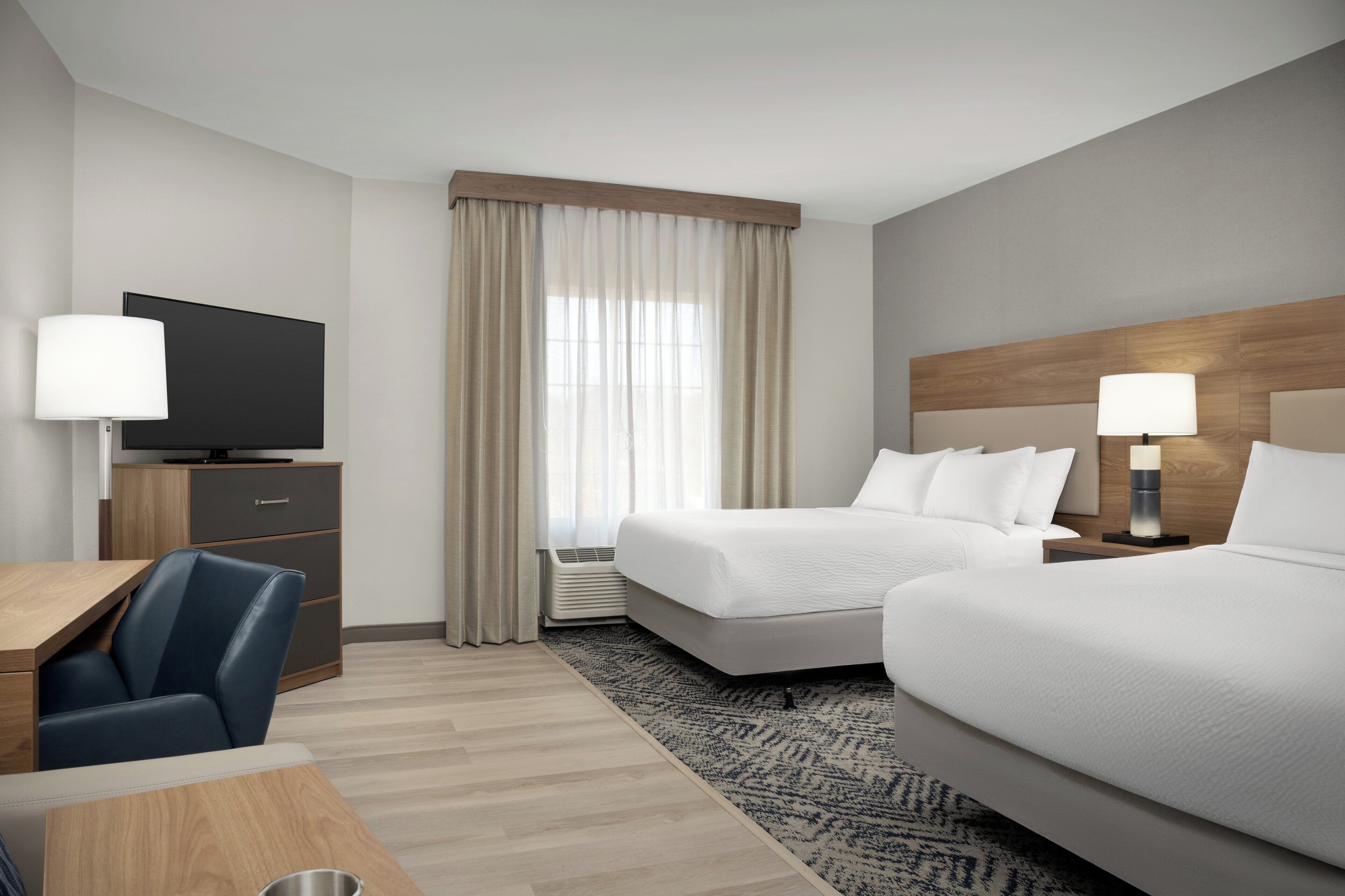 Ein Hotelzimmer mit einem Bett, einem Schreibtisch, einem Stuhl, einem Fernseher und einem Fenster mit Vorhängen.