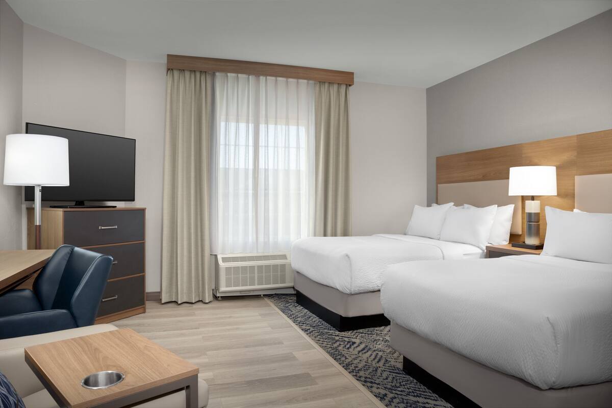 A hotel room with two beds, a desk, a chair, a TV, and a window with curtains.