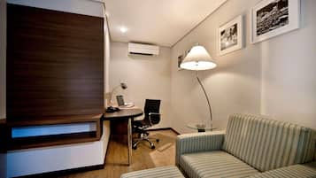Quarto de hotel moderno com parede de destaque em madeira, uma escrivaninha com um laptop, um sofá listrado e um abajur.