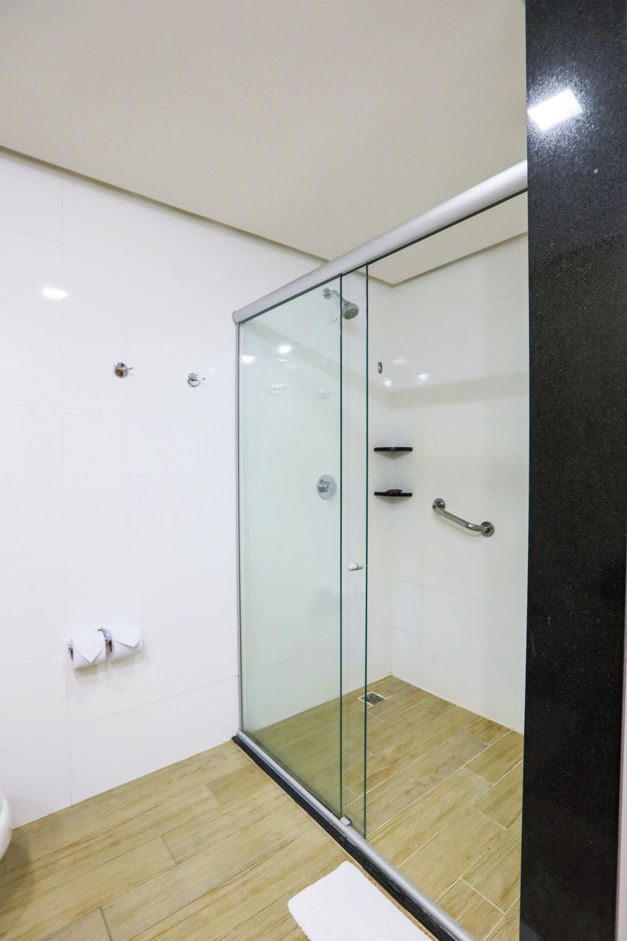 A modern bathroom with a glass shower enclosure, white tiles, and a wooden floor.