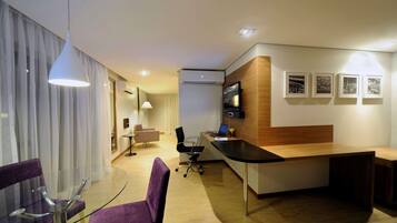 Habitación de hotel moderna con una mesa de comedor de cristal, sillas moradas, un mostrador de recepción de madera y una computadora portátil.