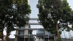 Un hotel moderno con fachada de vidrio, asientos exteriores y una entrada bordeada de árboles.