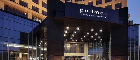 A hotel entrance with a modern facade, large glass windows, and a prominent sign reading "Pullman Hotels and Resorts".