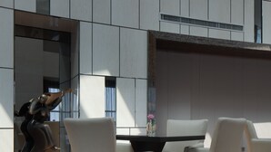 Un intérieur moderne avec un coin repas comprenant des chaises blanches et une table noire, de grandes fenêtres et une statue.
