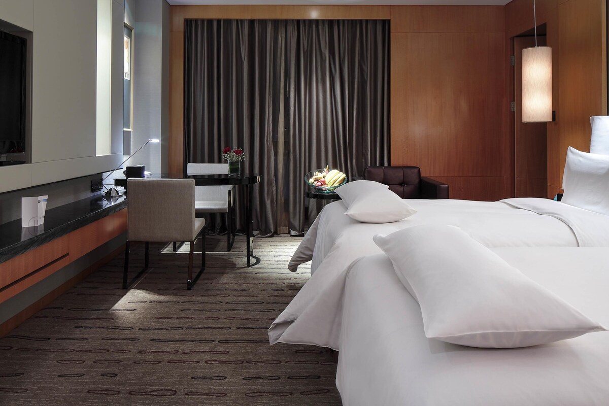 A hotel room with a bed, a desk, a chair, a mirror, and a curtain.