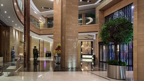A spacious lobby with a central circular light fixture, a reception desk, and a large potted plant. - Pullman Anshan Time Square (Anshan)