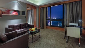 A modern hotel room with a leather sofa, a dining table, and a large window offering a city view at night. - Pullman Anshan Time Square (Anshan)