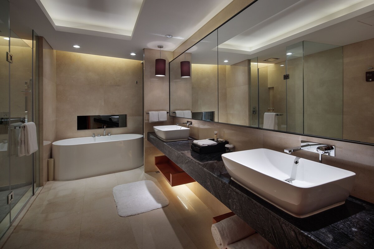 Un baño moderno con bañera, dos lavamanos, un espejo grande y una cabina de ducha de vidrio.