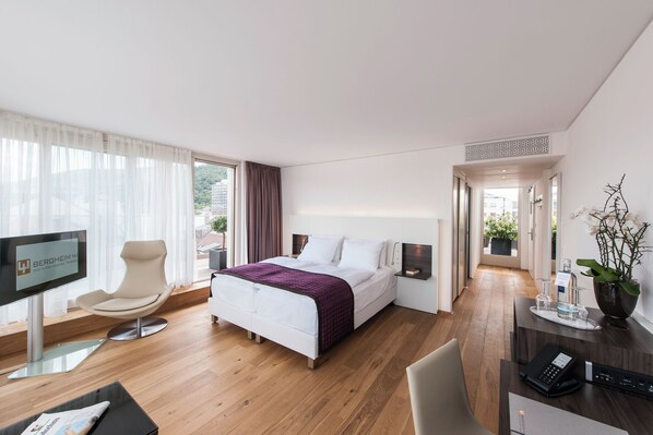 Una habitación de hotel moderna con cama, escritorio con teléfono, una silla, televisor y vista al exterior.