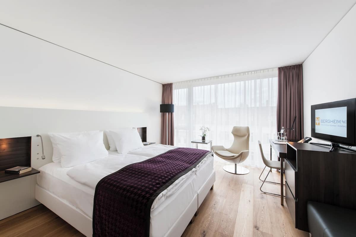 Una habitación de hotel con una cama, un escritorio con televisor, una silla y una ventana con cortinas.
