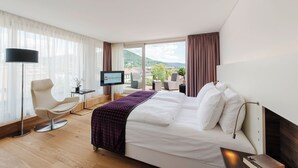 A hotel room with a bed, a desk, a chair, a TV, and a view of the outdoors.