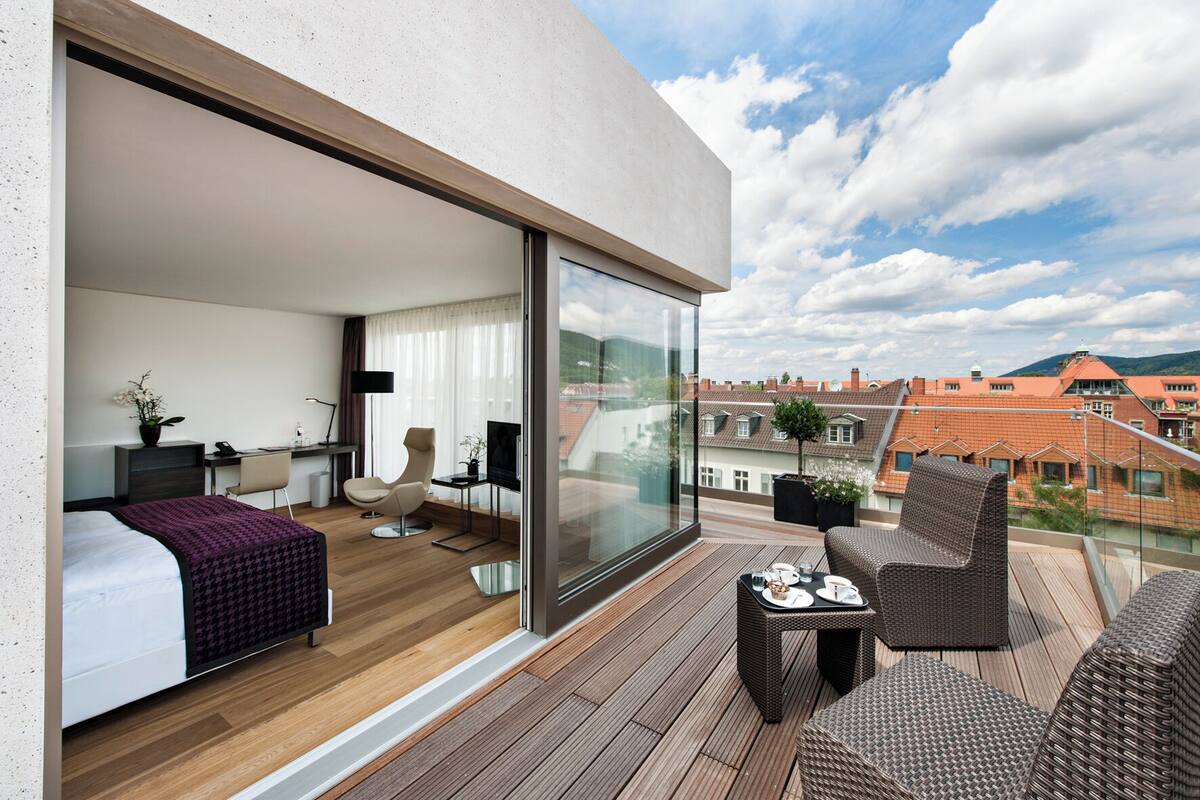Una habitación de hotel moderna con balcón, cama, escritorio, silla y televisor.