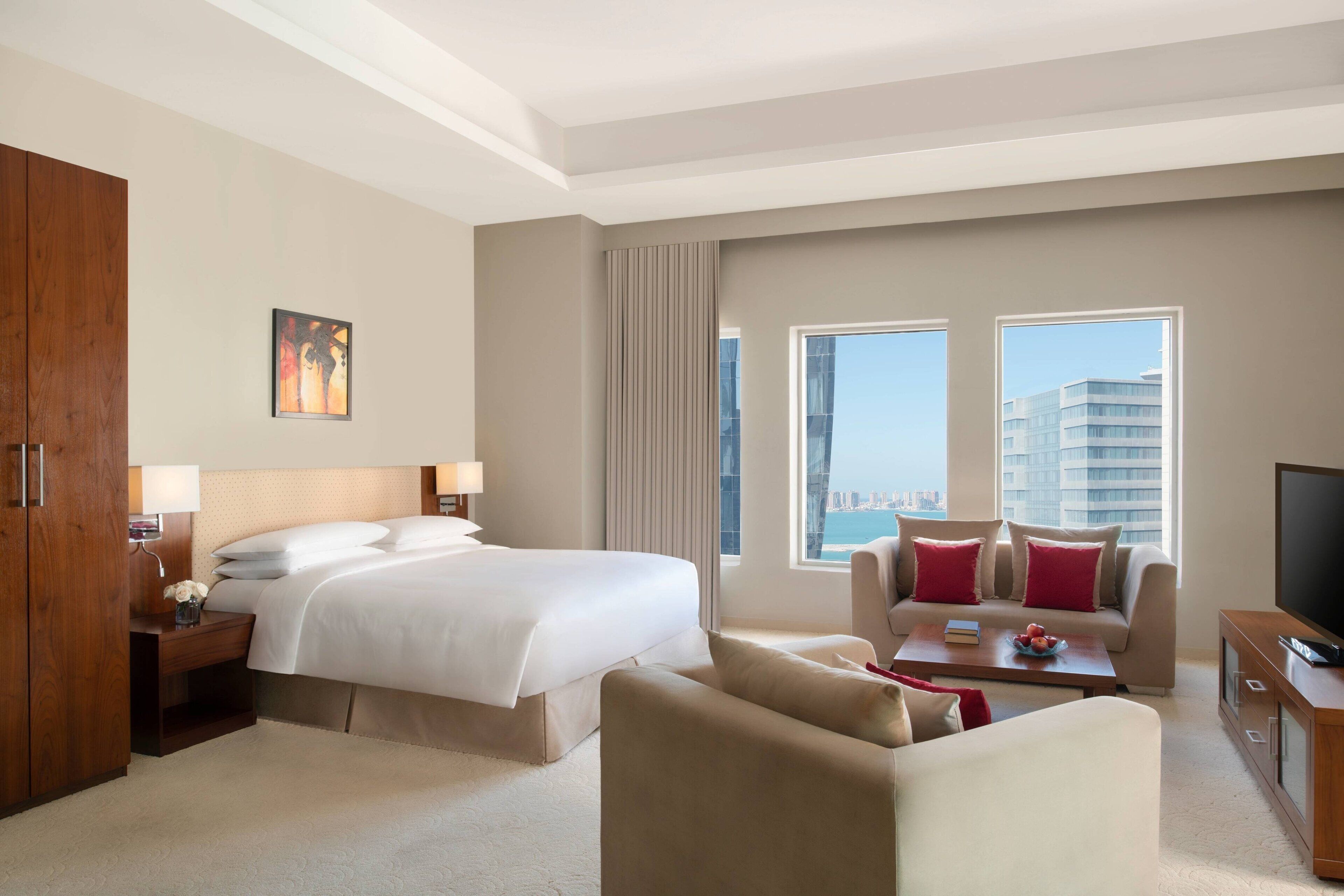 Habitación de hotel con una cama grande, un sofá, un televisor y vistas de la ciudad.