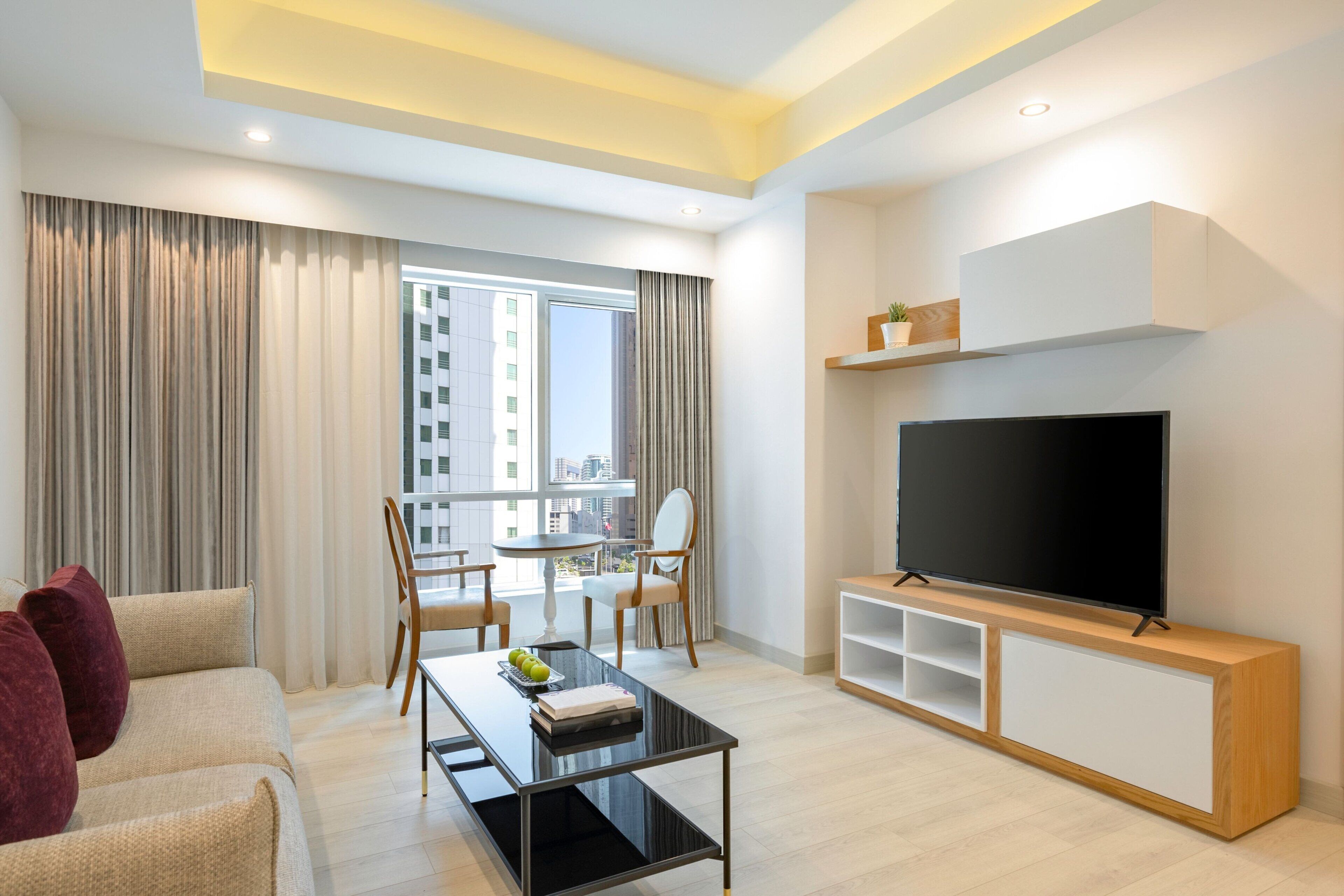 A modern living room with a sofa, a coffee table, a TV, and a balcony with curtains.