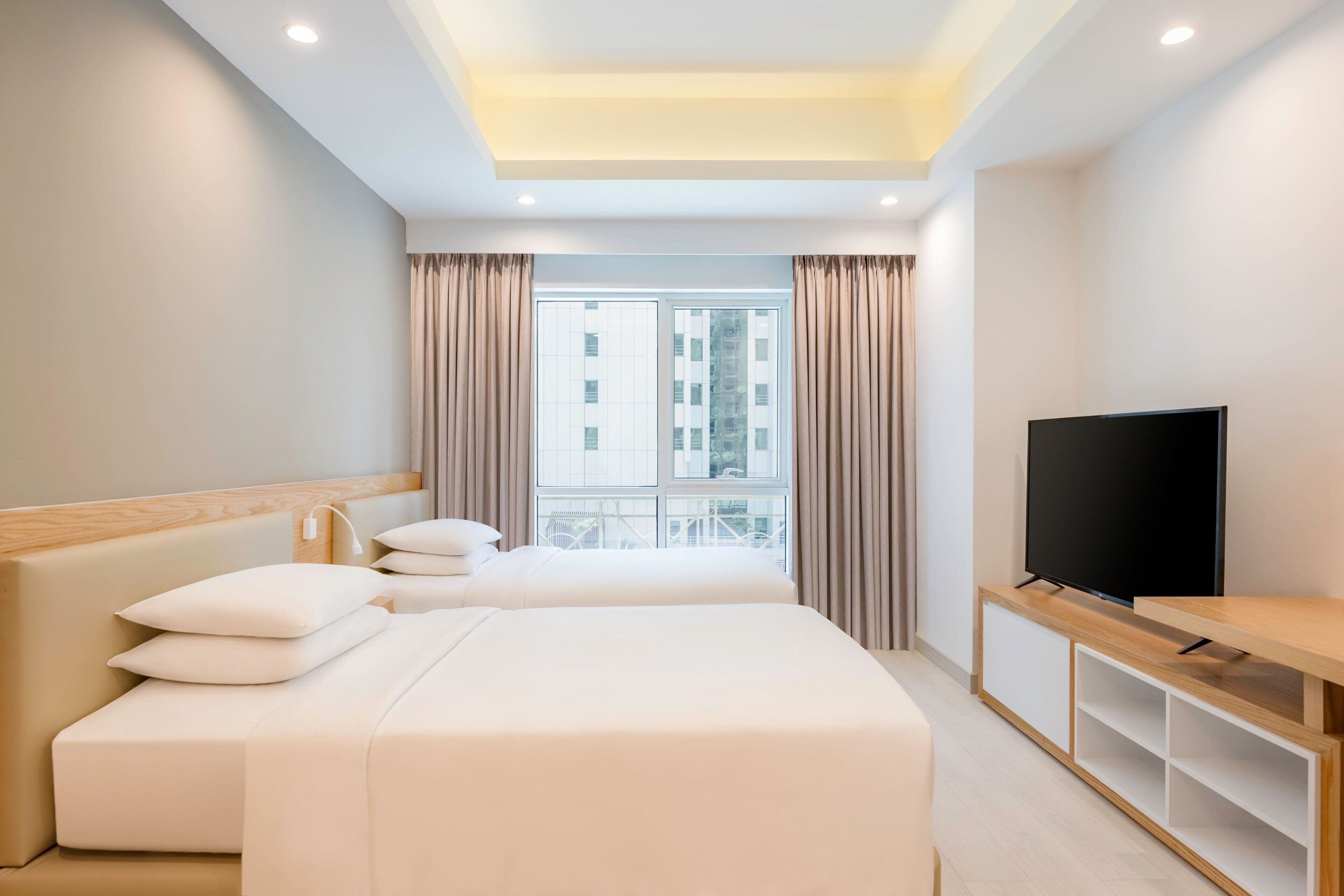 A hotel room with two beds, a TV, and a window with curtains.
