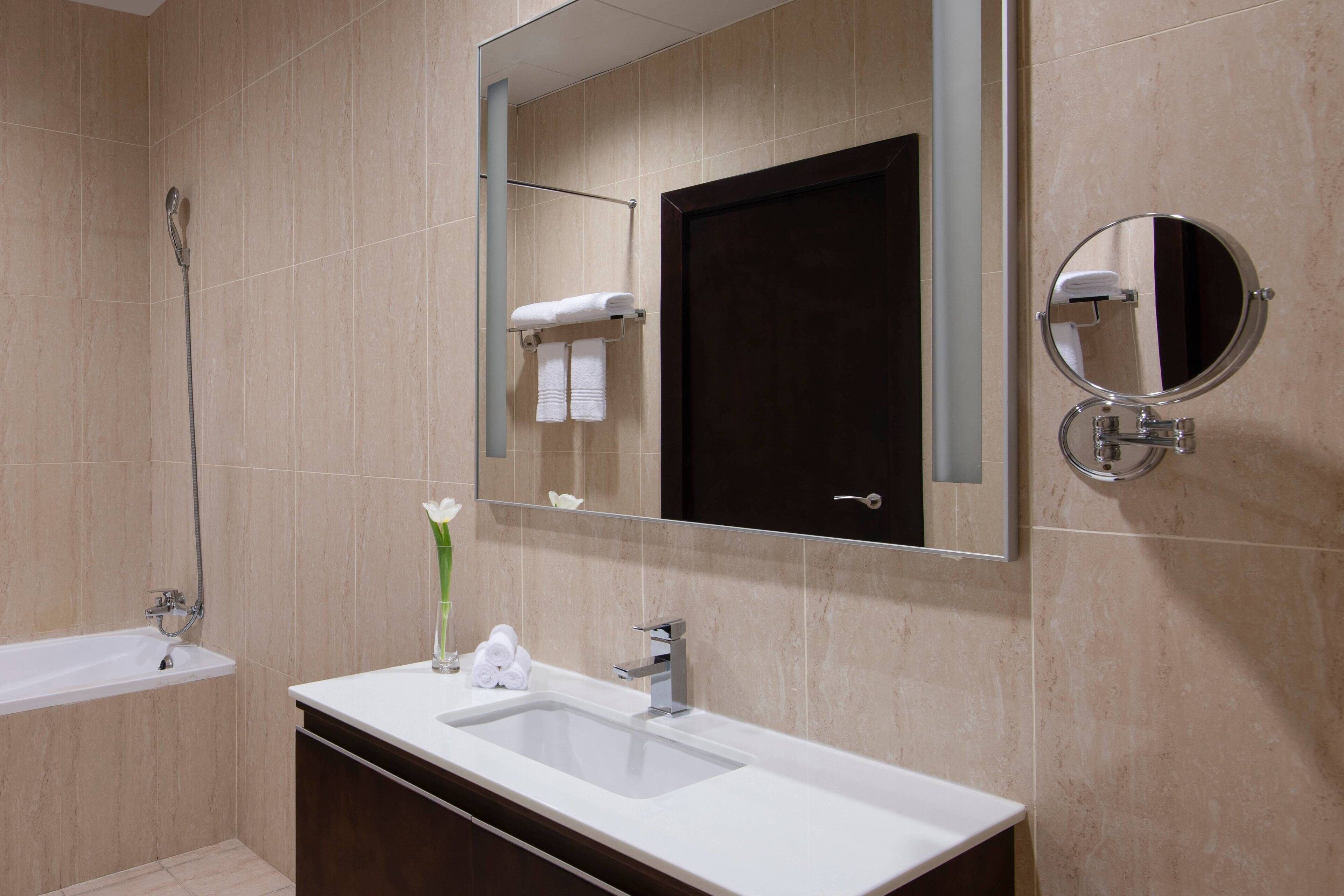 A modern bathroom with a bathtub, a sink, a mirror, and a towel rack.