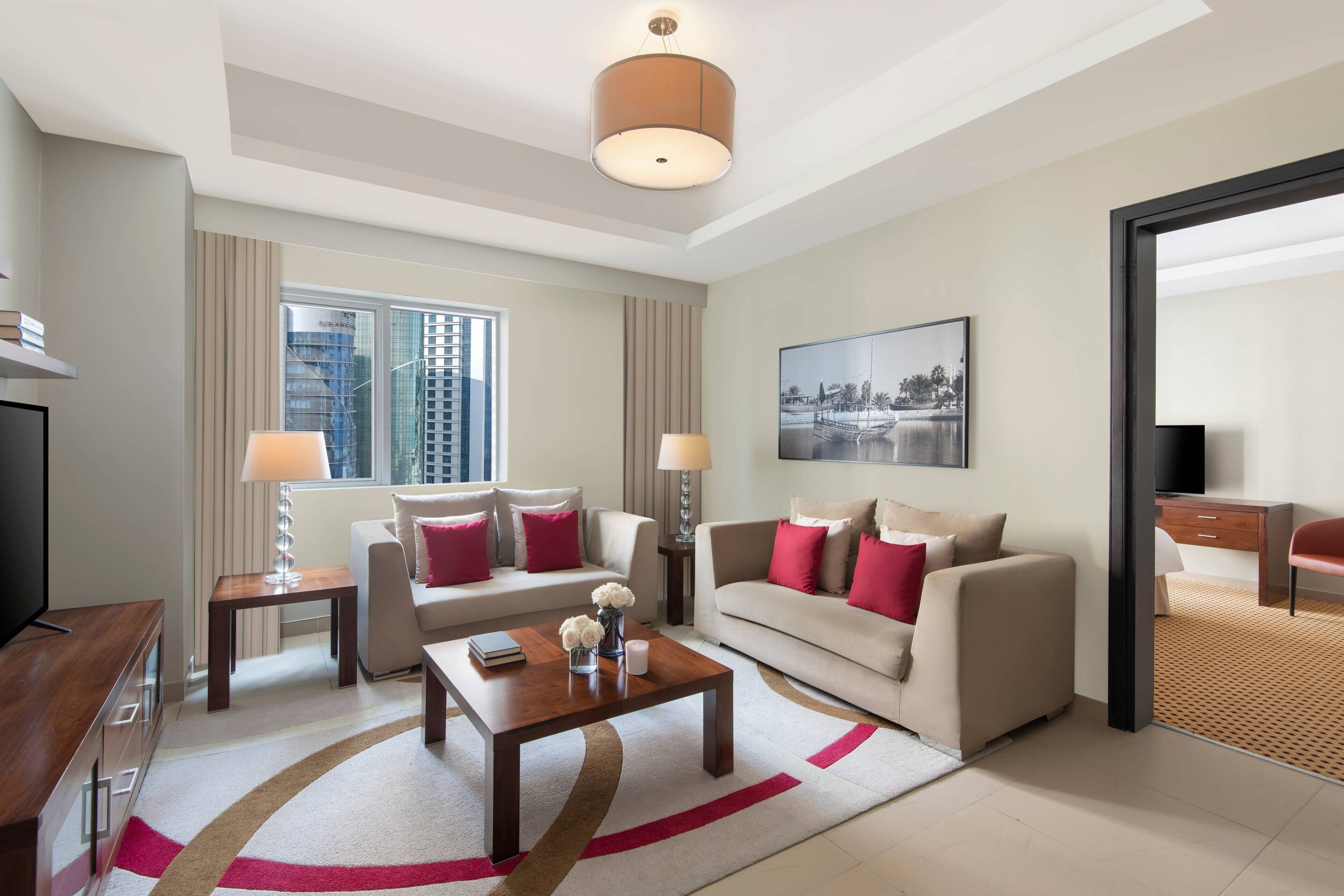 A modern hotel room with a sofa, two armchairs, a coffee table, and a TV.