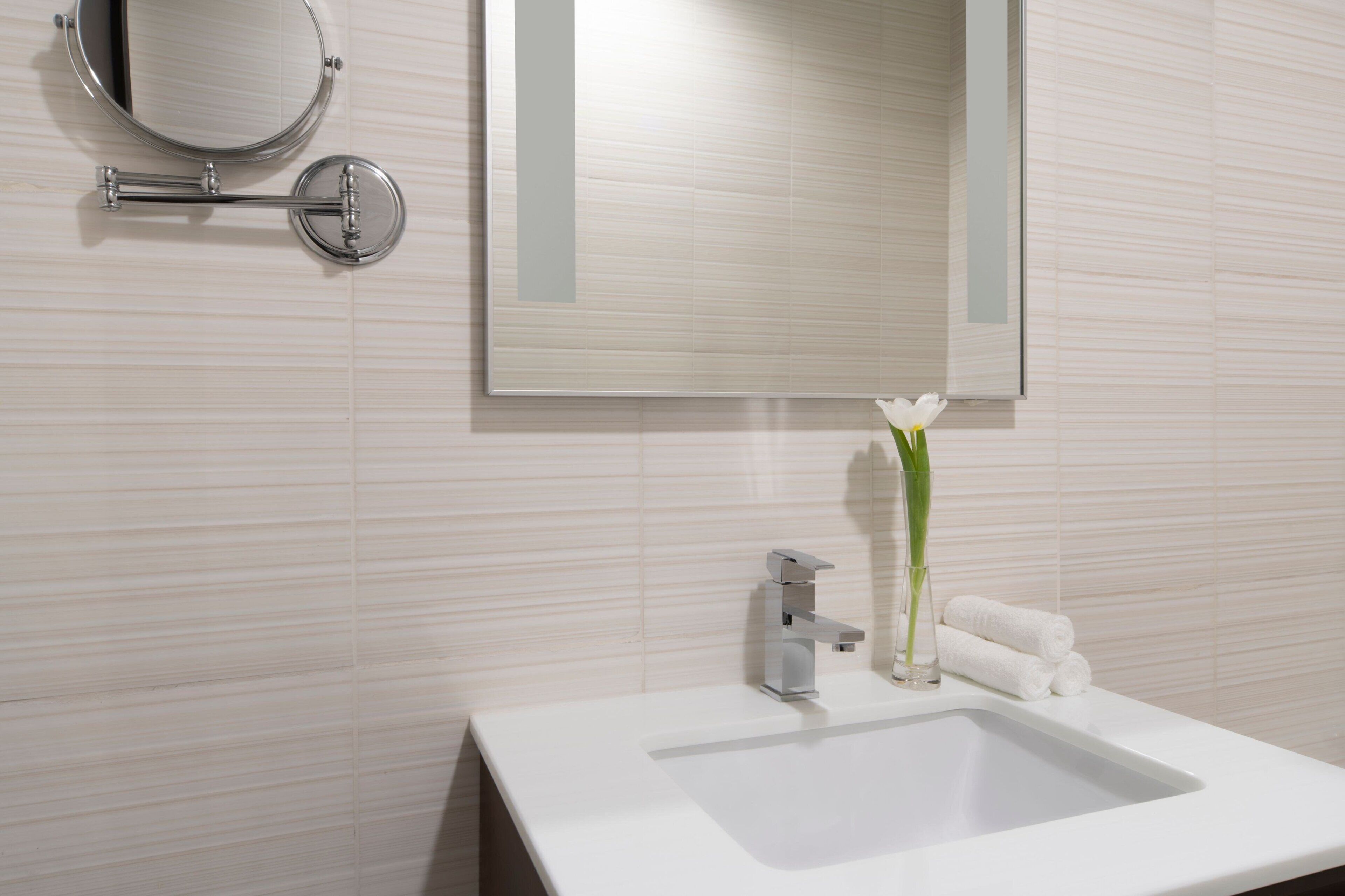A modern bathroom with a white sink, a mirror, and a vase with a single white flower.
