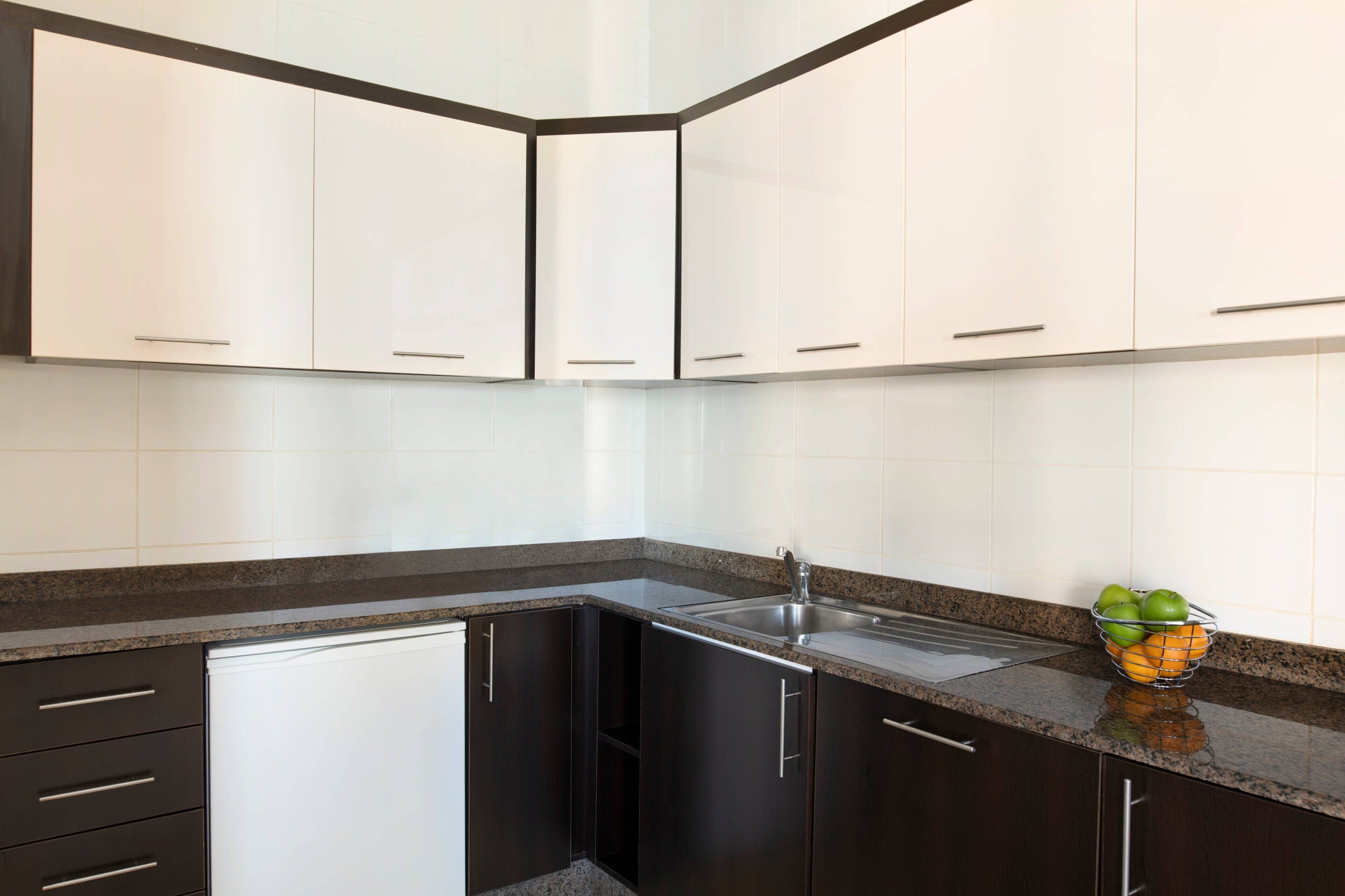Cocina con armarios oscuros, un refrigerador blanco y una encimera de granito.
