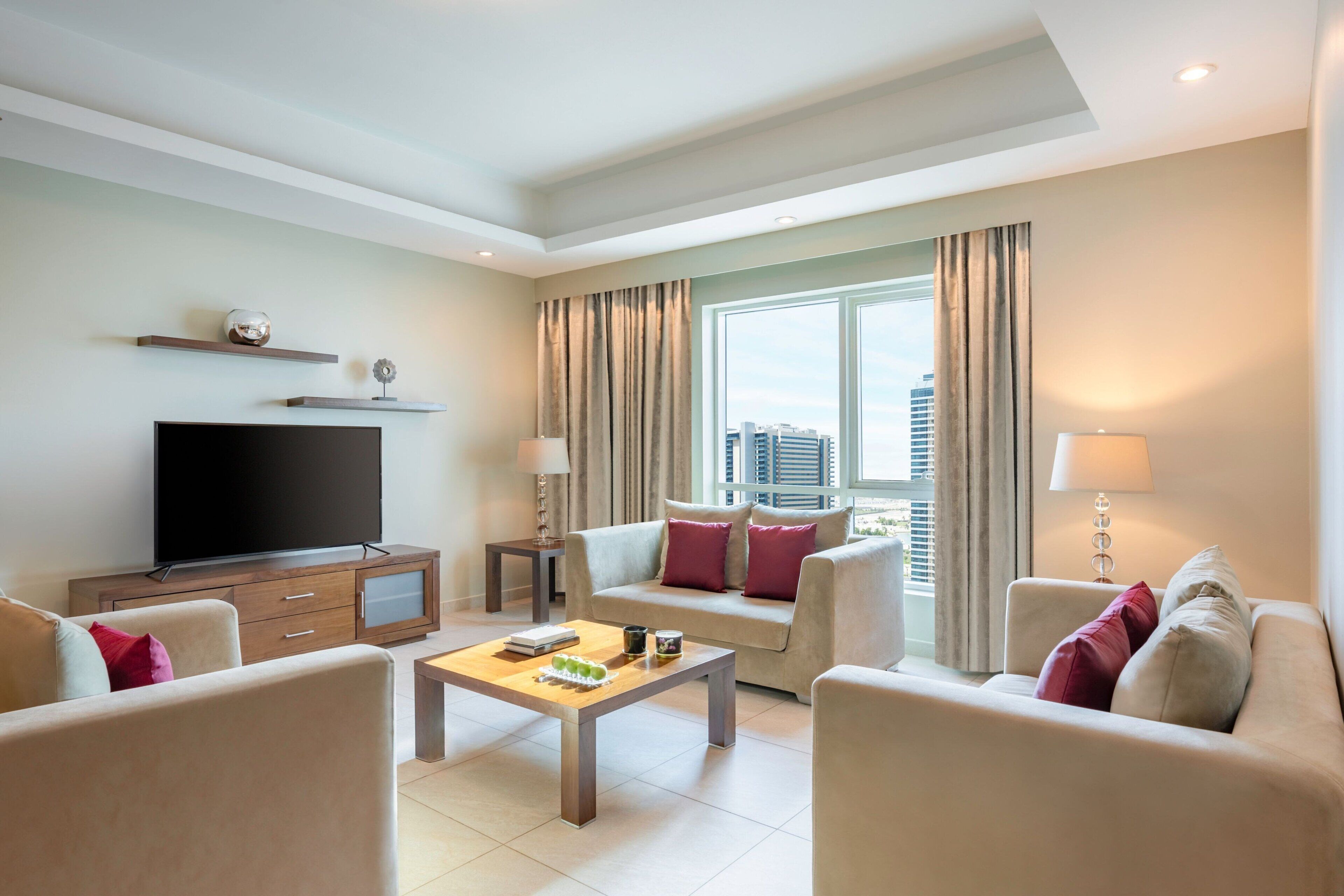 Una habitación de hotel moderna con televisión de pantalla plana, un sofá, una mesa de centro y un ventanal con cortinas.