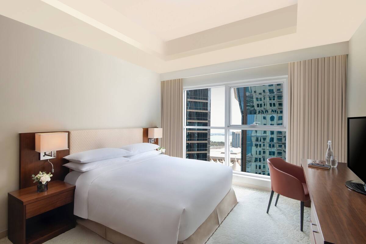 A hotel room with a large bed, a desk with a chair, a TV, and a window with a city view.