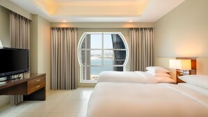 A hotel room with a large bed, a TV on a wooden desk, and a view of the sea through a large window. - Marriott Executive Apartments City Center Doha (Doha)