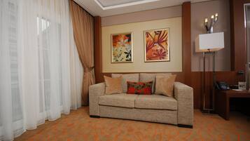 A hotel room with a sofa, a desk, a lamp, and two framed artworks on the wall.