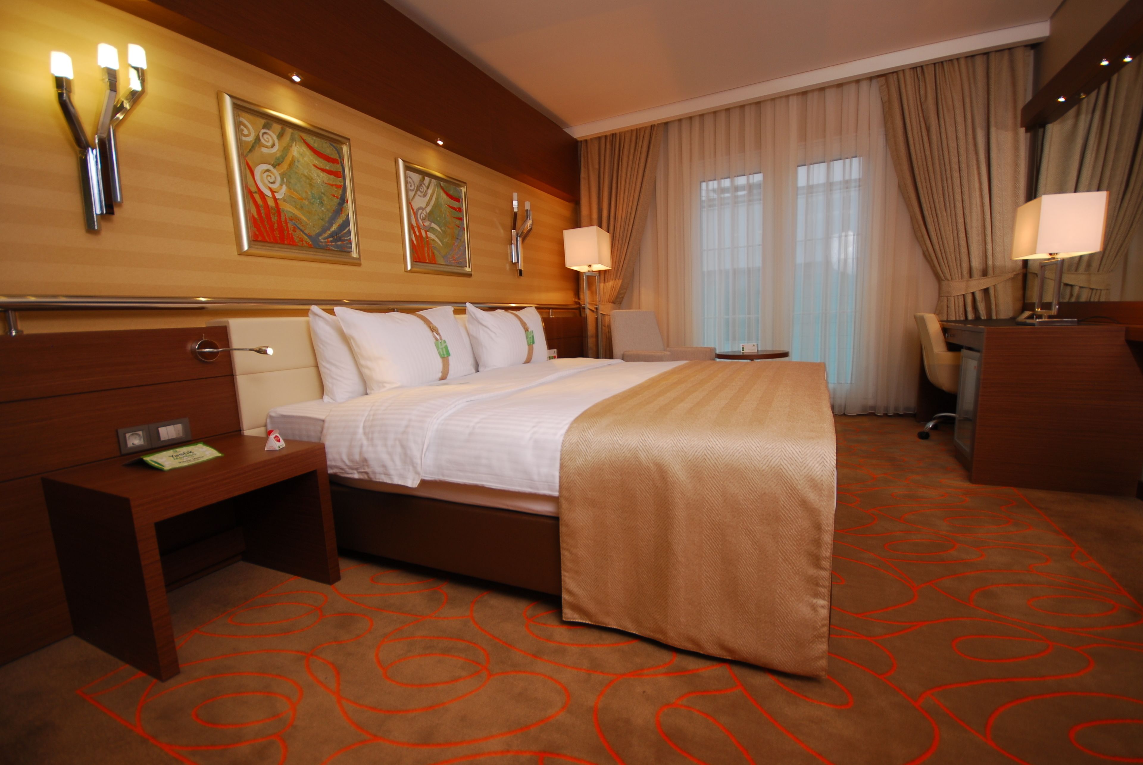 Una habitación de hotel con una cama grande, un escritorio, una silla y una lámpara de escritorio.