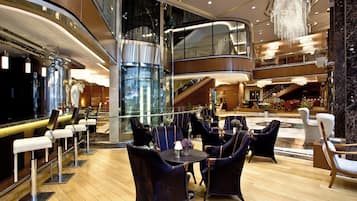 Un hall d’hôtel moderne doté d’un bar, de coins salon et d’un ascenseur en verre.