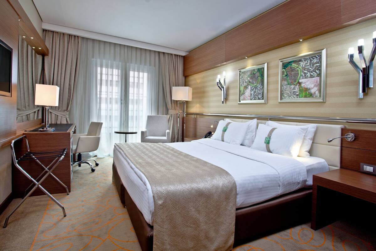 A hotel room with a large bed, a desk, a chair, a small table, and a TV.