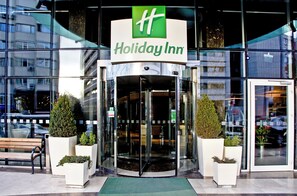 A Holiday Inn hotel entrance with a glass revolving door, potted plants, and a bench outside. - Holiday Inn Ankara - Kavaklidere by IHG (Ankara)