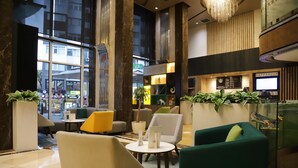 A modern lobby with seating areas, a reception desk, and large windows offering a view of the street.