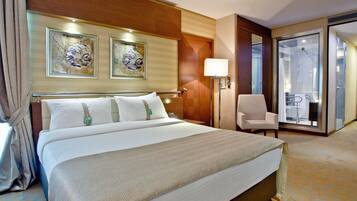 A hotel room with a large bed, a chair, a desk, and a bathroom visible through a glass door.