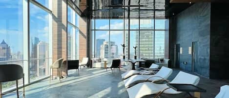A modern lounge with large windows, a city view, and a mix of seating options.