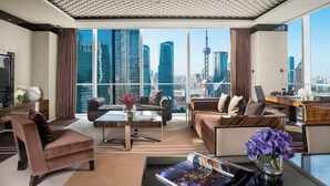 A modern living room with a city view, featuring a sofa, a coffee table, and a desk with a chair. - Regent Shanghai Pudong (Shanghai)