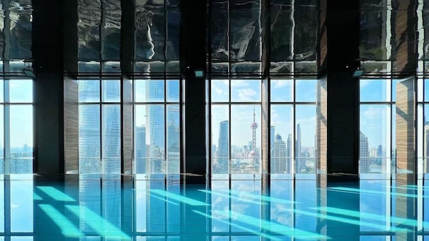 A modern indoor swimming pool with large windows offering views of a city skyline. - Regent Shanghai Pudong (Shanghai)