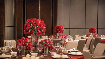 A dining area with round tables set for a meal, each with a centerpiece of red roses in a clear vase.