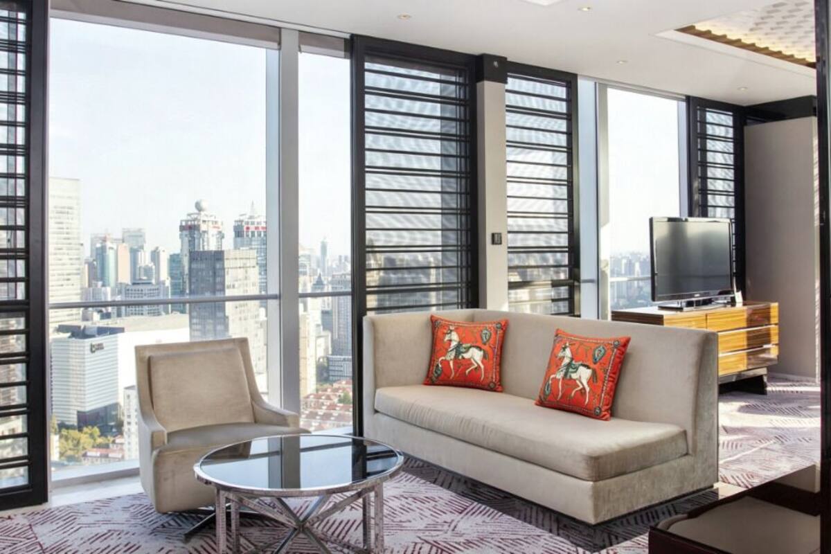 A modern hotel room with a large window, a sofa with decorative pillows, a television, and a small table.