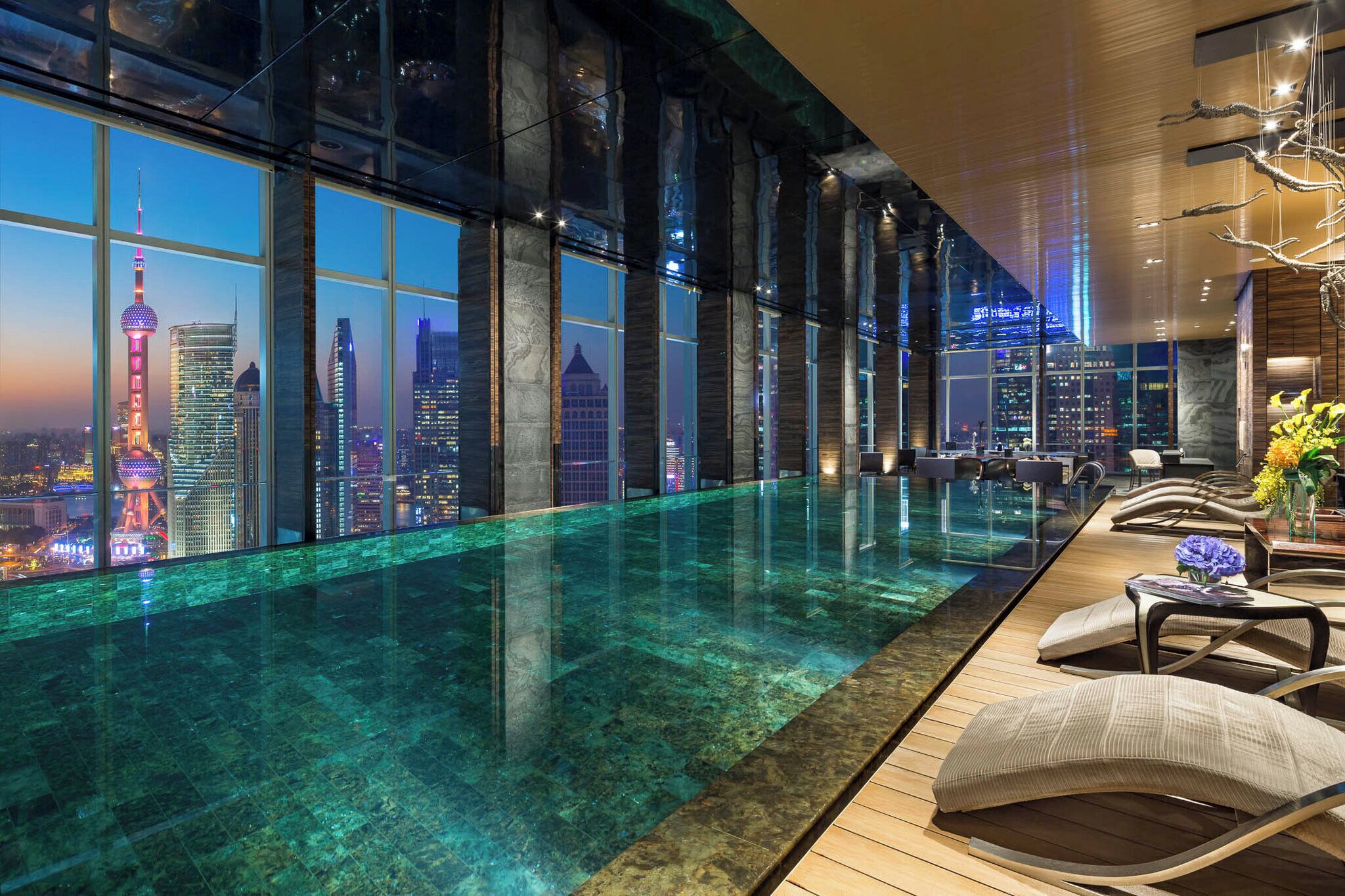 Una habitación de hotel moderna con un gran ventanal que ofrece vistas a la ciudad, una piscina infinita y un área de descanso con vistas.