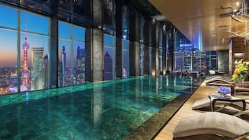 Una habitación de hotel moderna con un gran ventanal que ofrece vistas a la ciudad, una piscina infinita y un área de descanso con vistas.