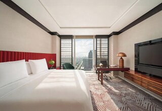 A hotel room with a large bed, a desk with a lamp, a TV, and a view of the cityscape.