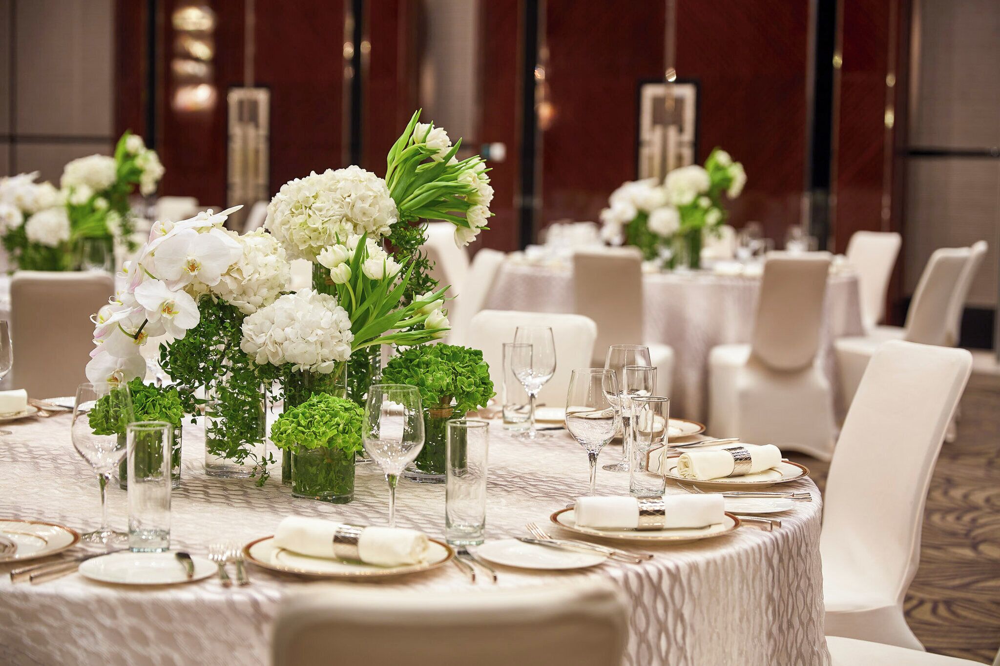 Una mesa de banquete dispuesta con flores blancas, copas de cristal y servilletas blancas dobladas con cuidado.