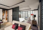 A modern hotel room with a large bed, a sitting area with a sofa, a desk, and a view of the city through large windows.