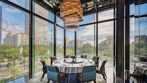 A round dining table with chairs, set for six, in a room with large windows offering a city view. - Regent Shanghai Pudong (Shanghai)