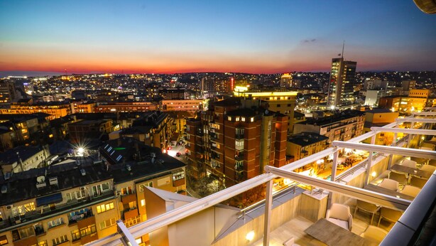 Un edificio de gran altura con varios pisos, balcones y vistas a un paisaje urbano al atardecer.