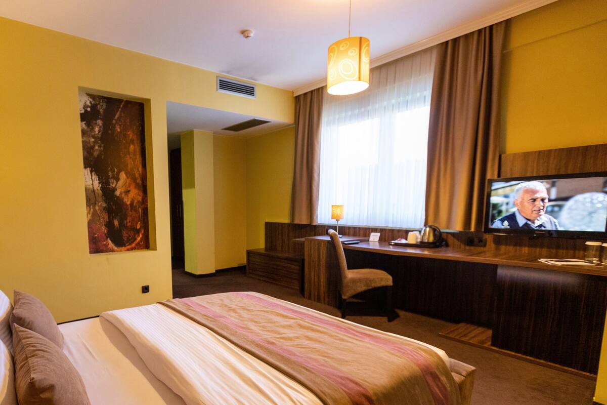 A hotel room with a bed, a desk, a chair, a television, and a painting on the wall.