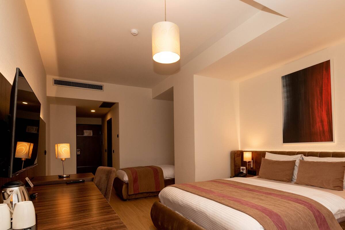 A hotel room with a bed, bedside tables, a TV, and a mirror.